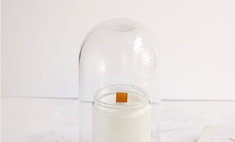 A wood-wick candle beneath a glass cloche